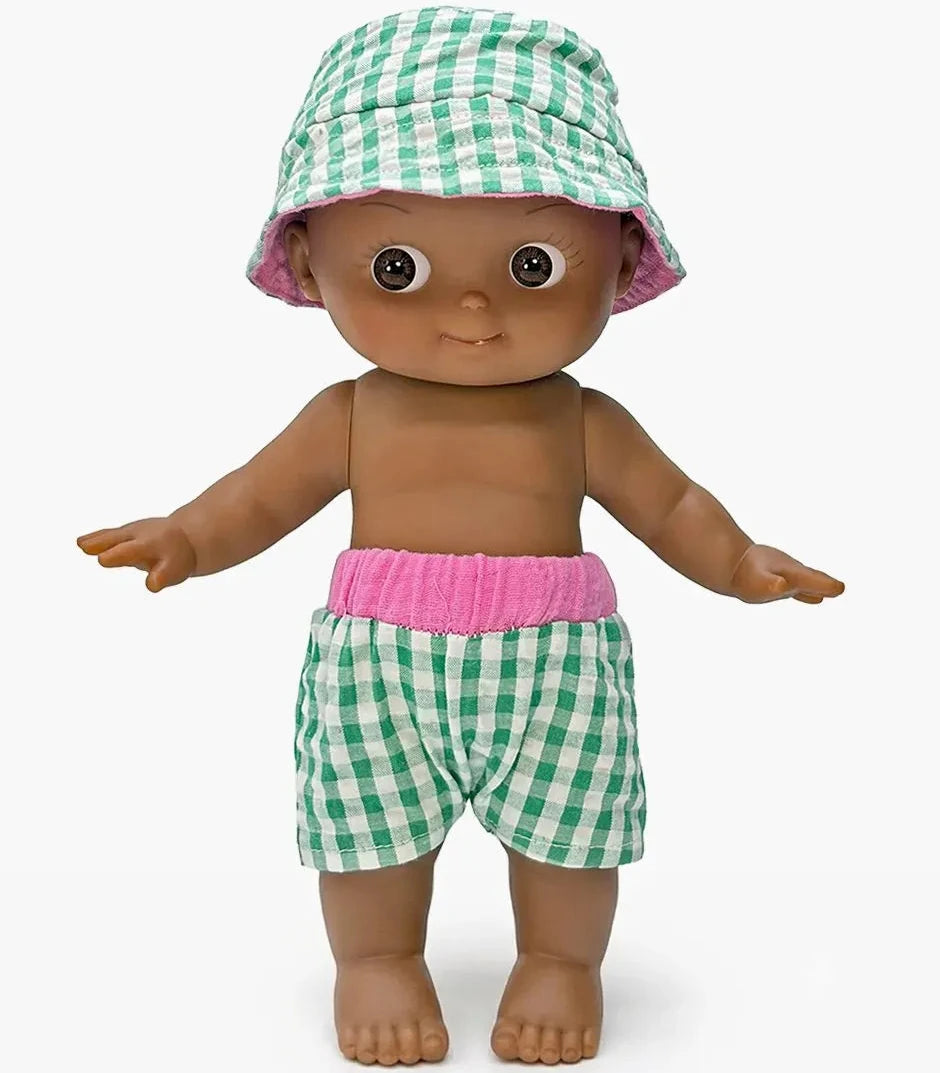 A baby doll with brown skin and large eyes, wearing a green and white gingham bucket hat and matching gingham shorts with a pink waistband, standing against a light gray background.