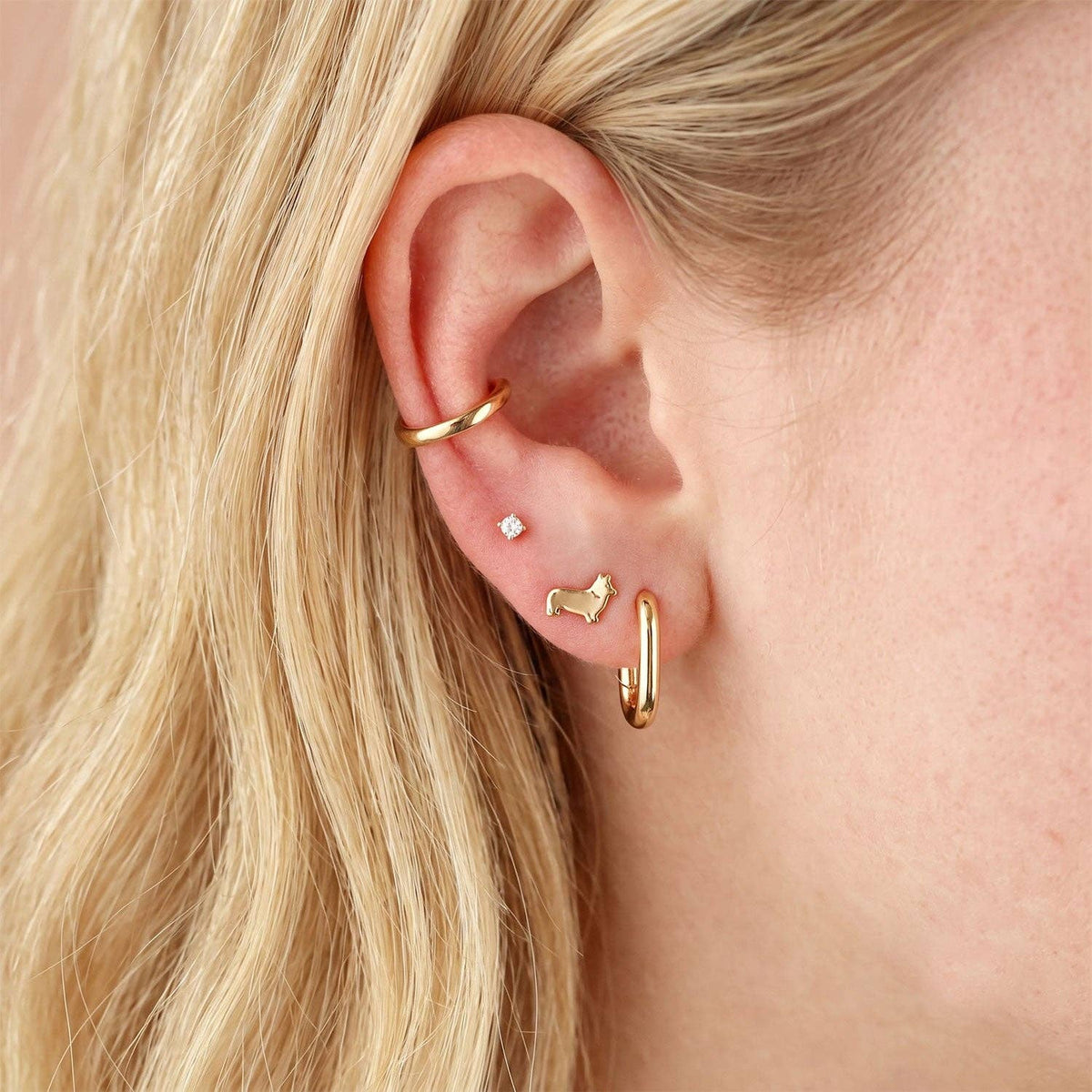 Close-up of an ear wearing gold hoop earrings with a small stud and a charm.