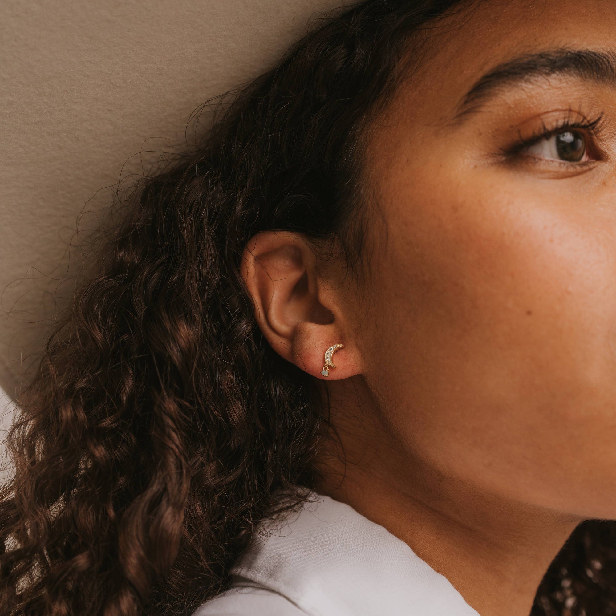 Pair of gold moon stud earrings on a white card with text on a beige background