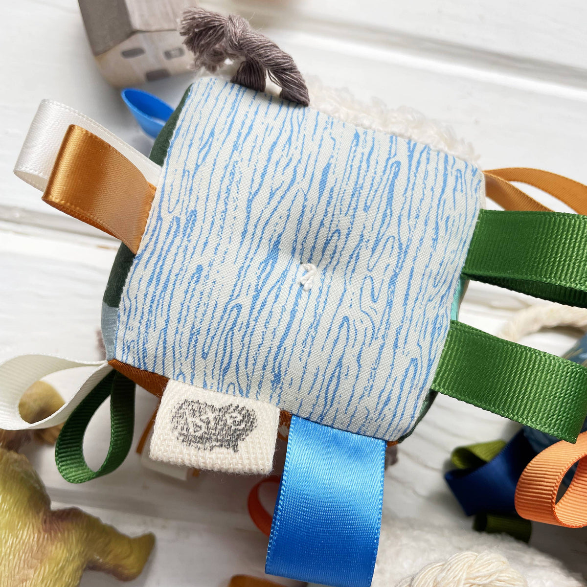 Patterned fabric square with ribbons and a small animal figure on a white surface