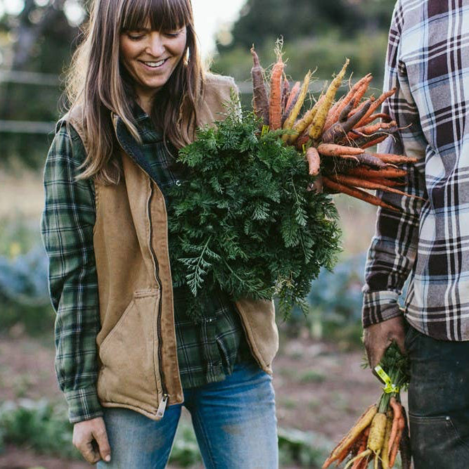Two people holding bunches of fresh vegetables in a garden setting