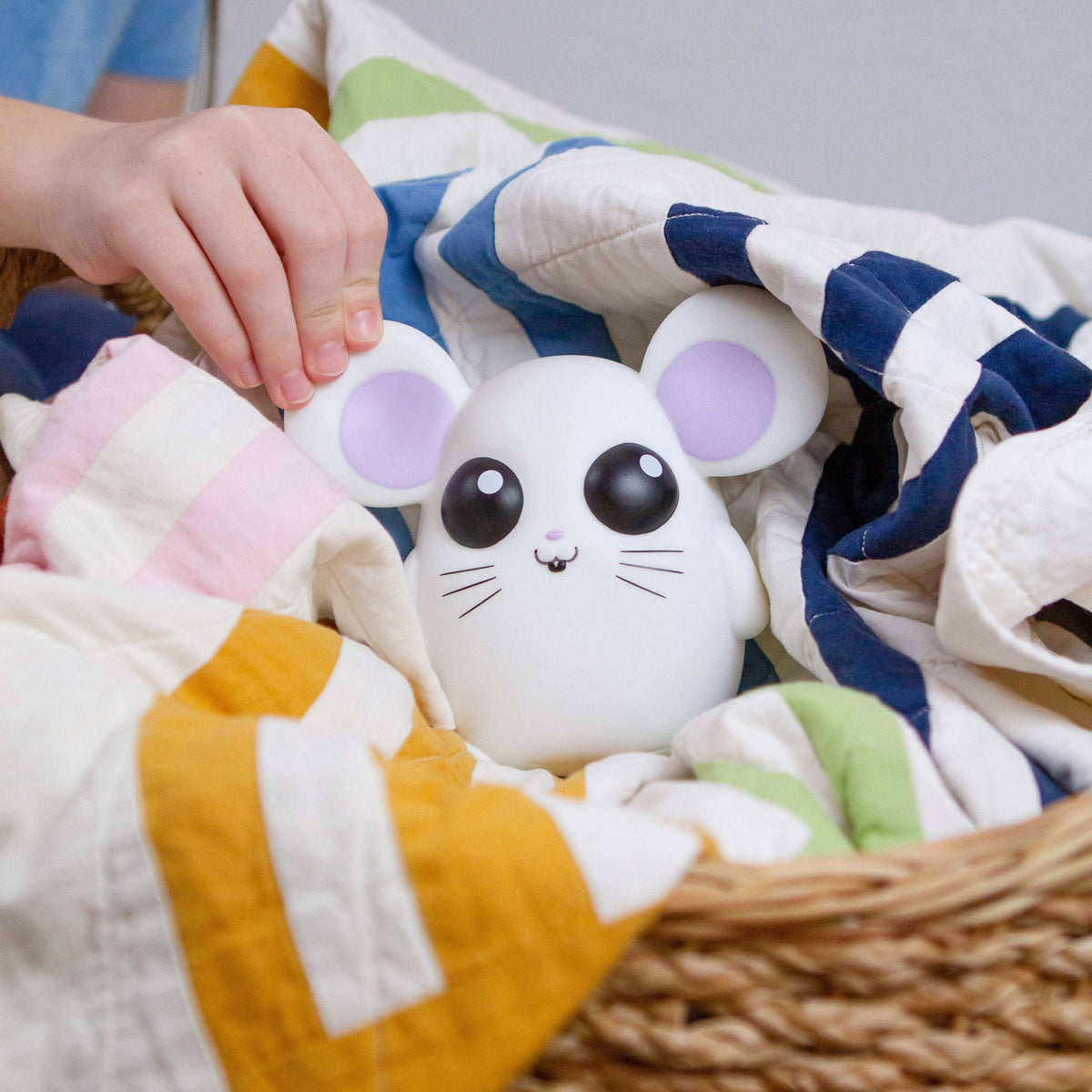 White plush toy with purple accents in a basket of colorful cloths