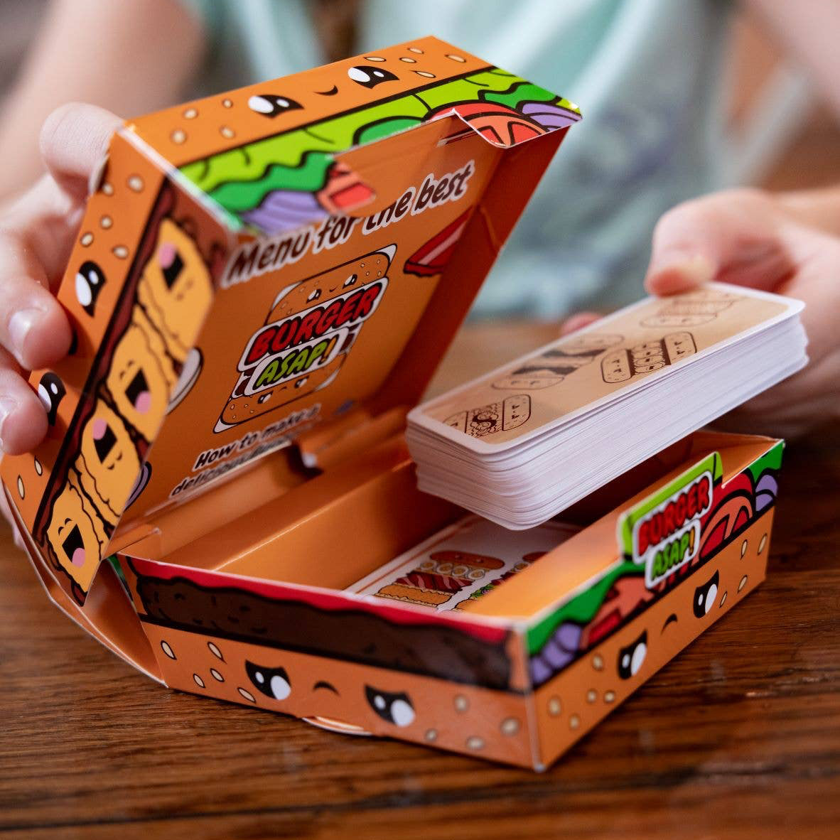 Card game packaging with cards being pulled out, on a wooden surface.