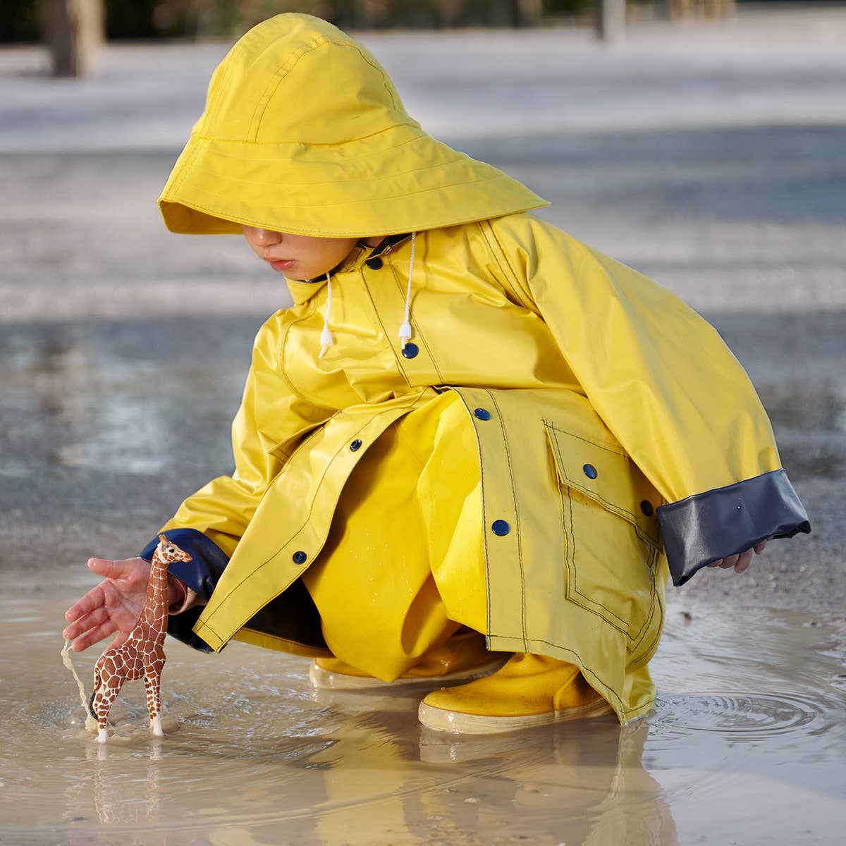 Person in a yellow raincoat playing with a toy in a puddle