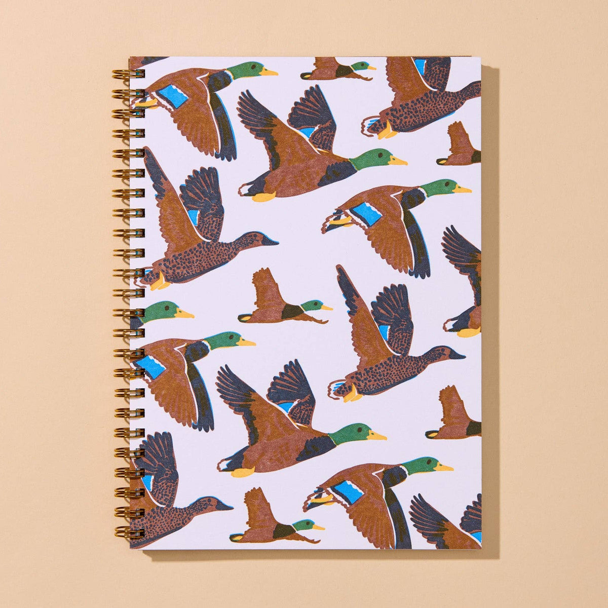A spiral-bound notebook with a white cover printed with a repeating pattern of flying mallards in brown, green, blue, and yellow, set against a solid beige background.