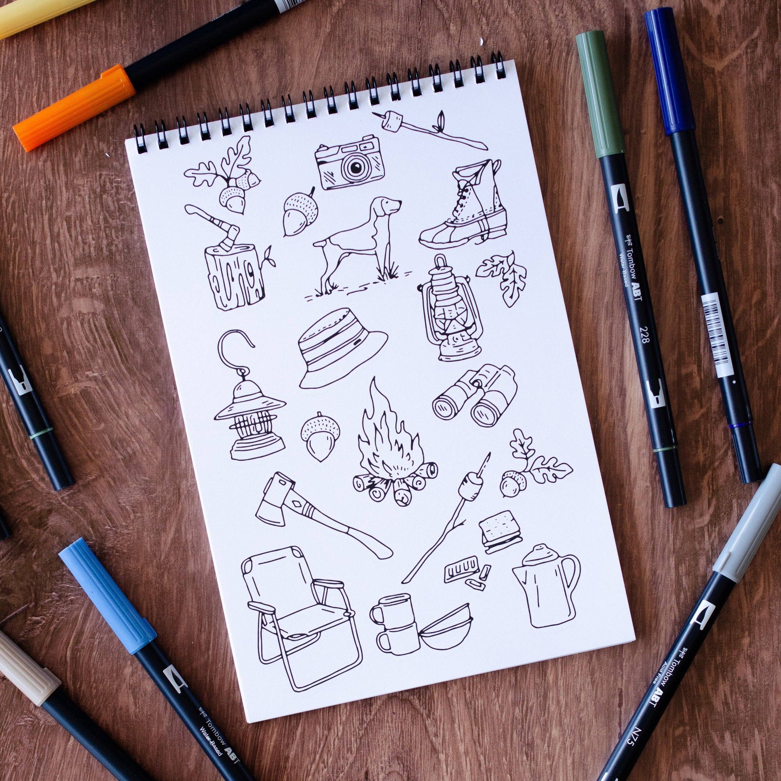 Coloring book titled 'The Great Outdoors' on a wooden surface with markers around it.