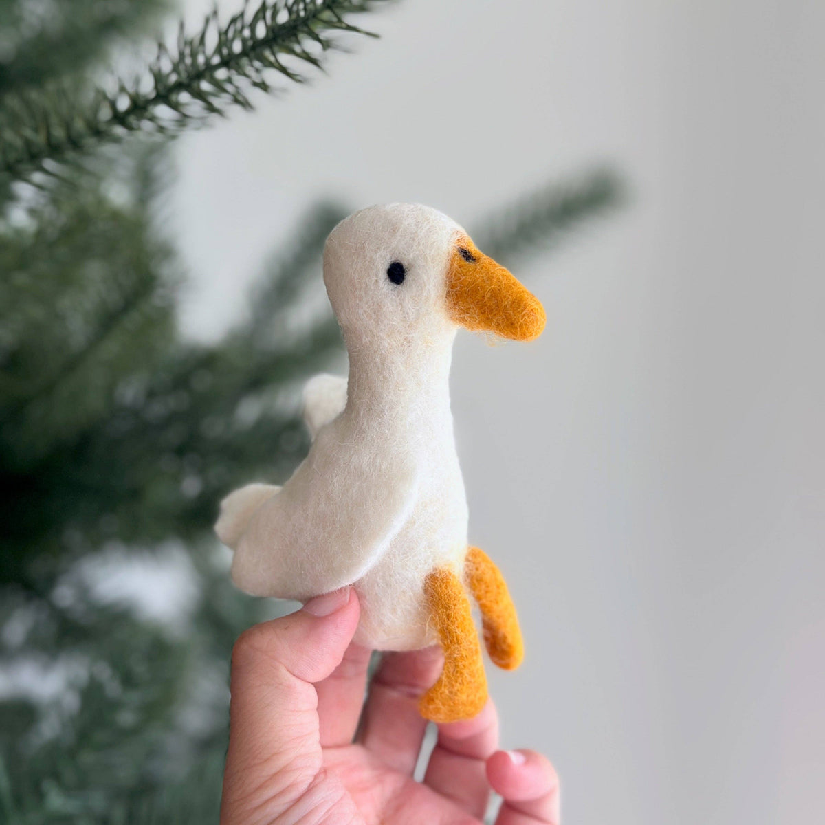 Hand holding a small felt goose ornament against a blurred natural background
