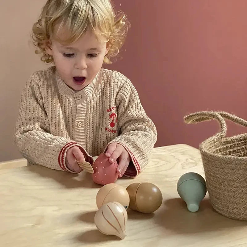 Child playing with wooden toys on a wooden table against a pink wall.