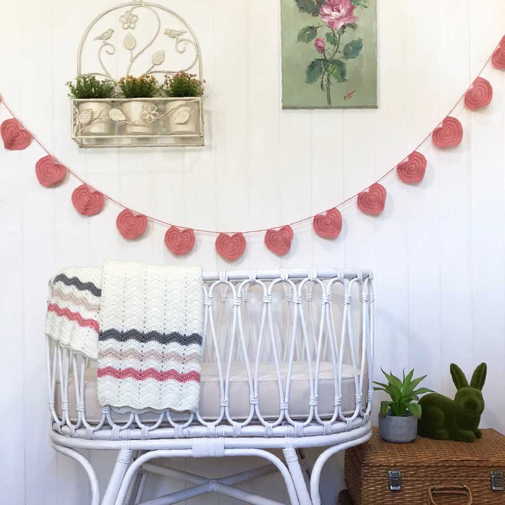 White crib with a striped blanket in a room decorated with a flower garland and wall art.