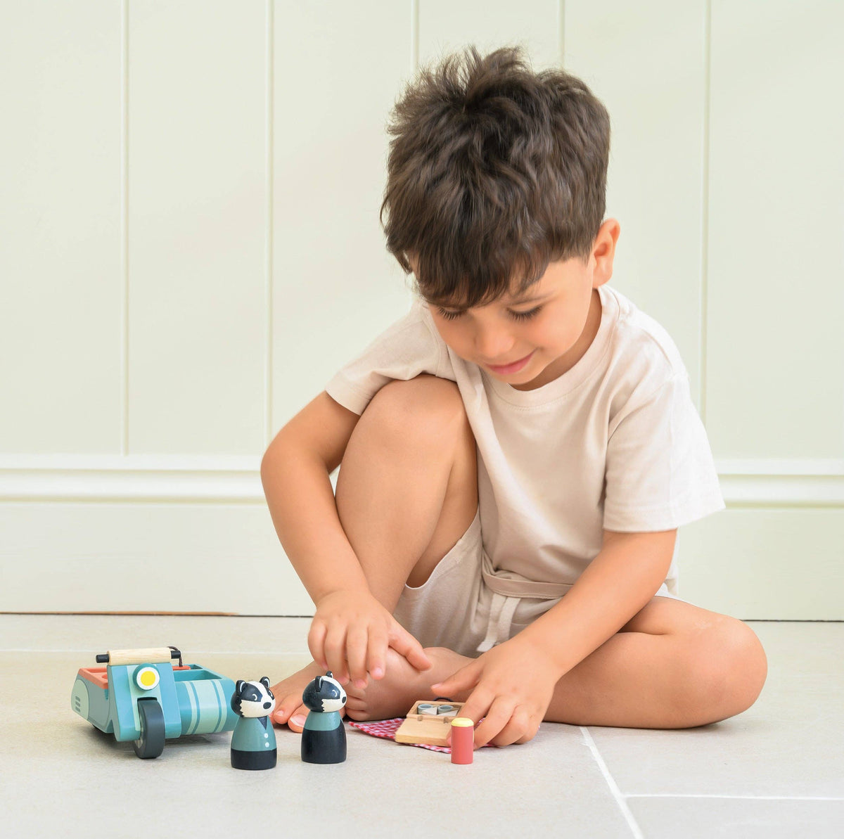 Child playing with toy cars and figurines on a light surface.