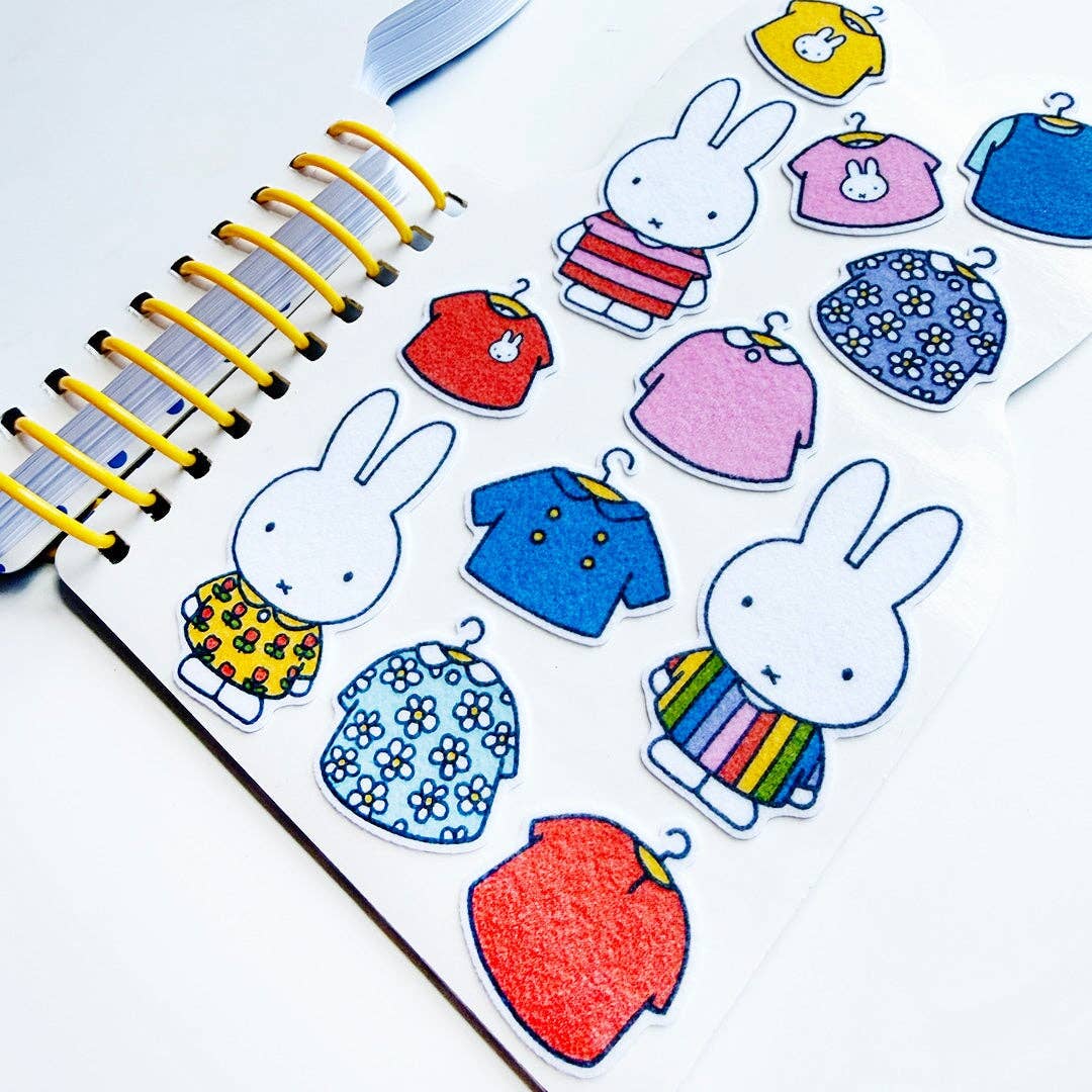Stickers of cartoon bunnies and colorful clothing on a notebook page.