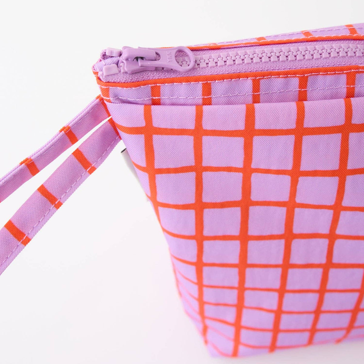 A close-up of a small zip pouch with a lavender and orange grid pattern, featuring a matching wrist strap and a lavender zipper pull.