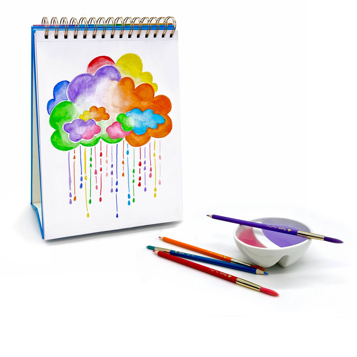 Colorful cloud drawing on a spiral-bound notebook with paintbrushes and a bowl of paint on a white background