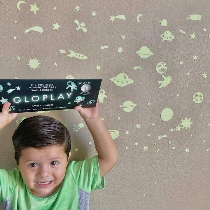Child holding a GloPlay product against a wall with glow-in-the-dark stickers.