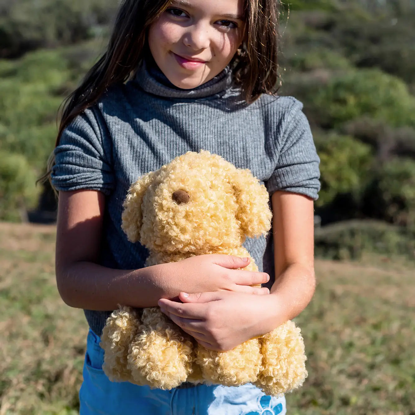A child holding a beige plush toy designed to look like a labradoodle dog.