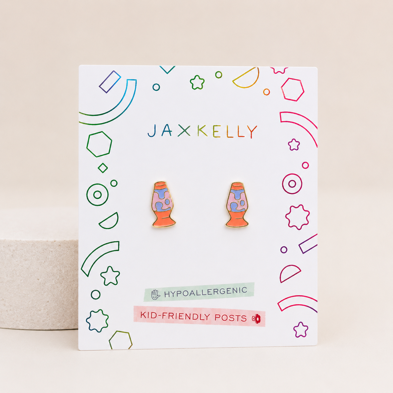A pair of Jaxx Kelly brand kid-friendly lava lamp enamel pins displayed on their white backing card, which features colorful geometric line art and text indicating they are hypoallergenic and kid-friendly.