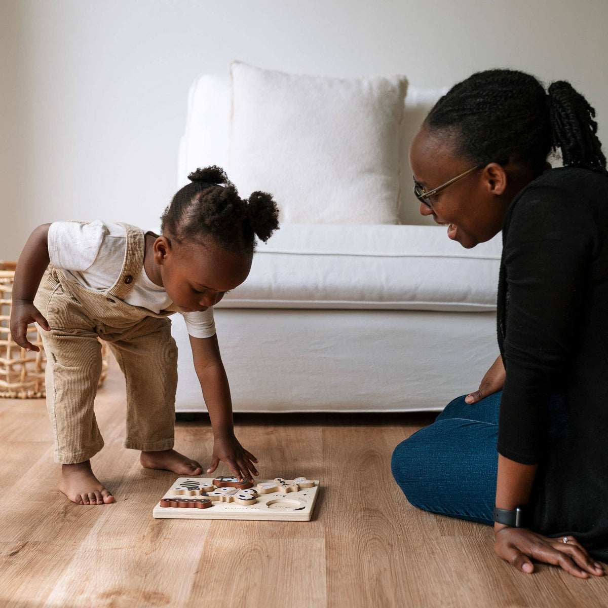 Woman and child playing with a puzzle on a wooden floor.