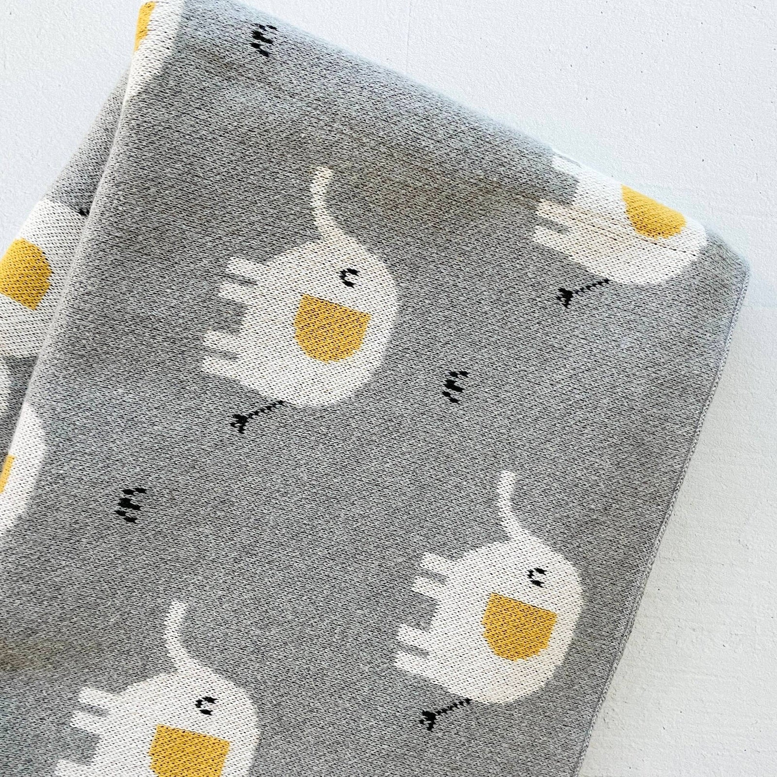 Gray blanket with white and yellow cat pattern on a white background