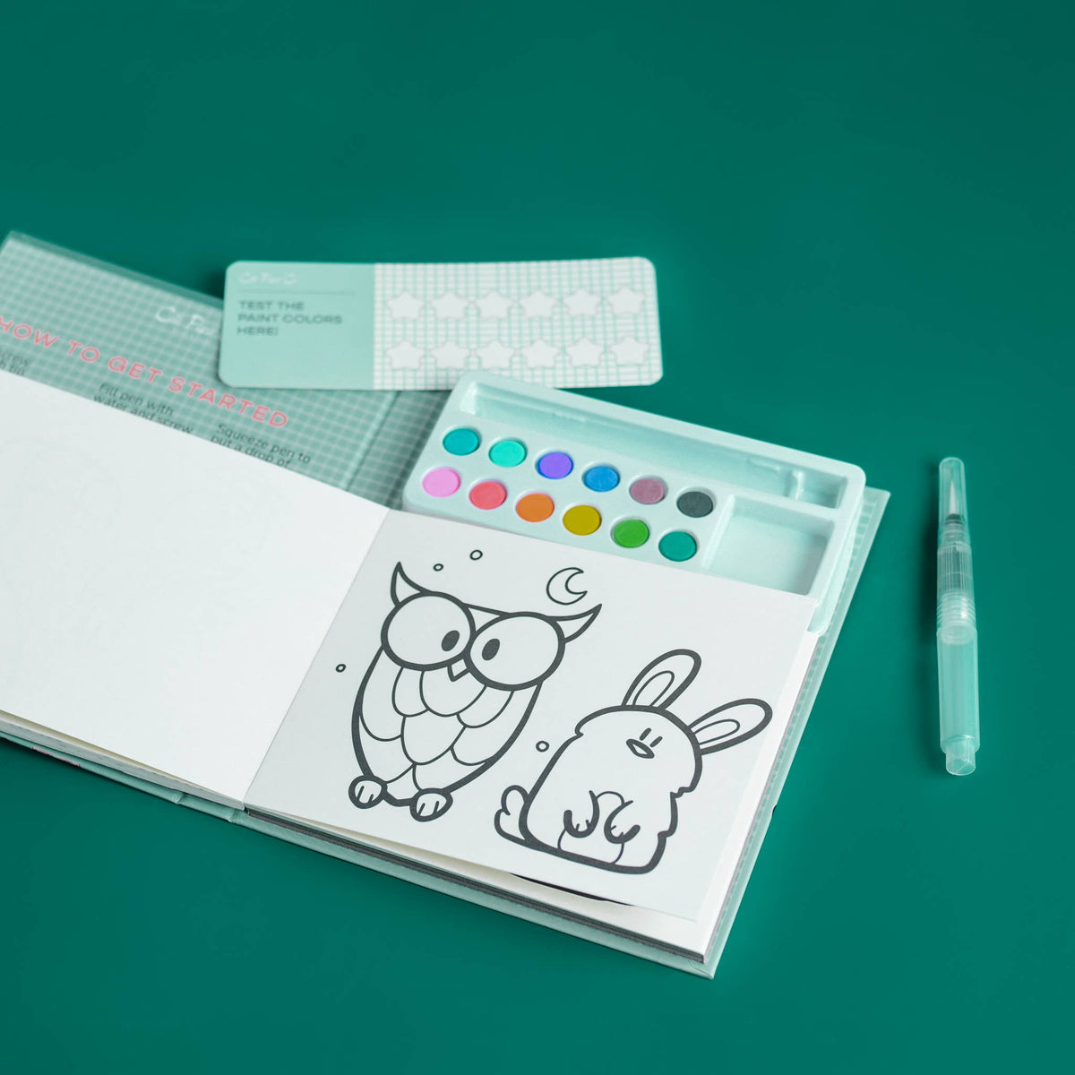 Coloring book with owl and rabbit illustrations, watercolor palette, and tools on a teal background