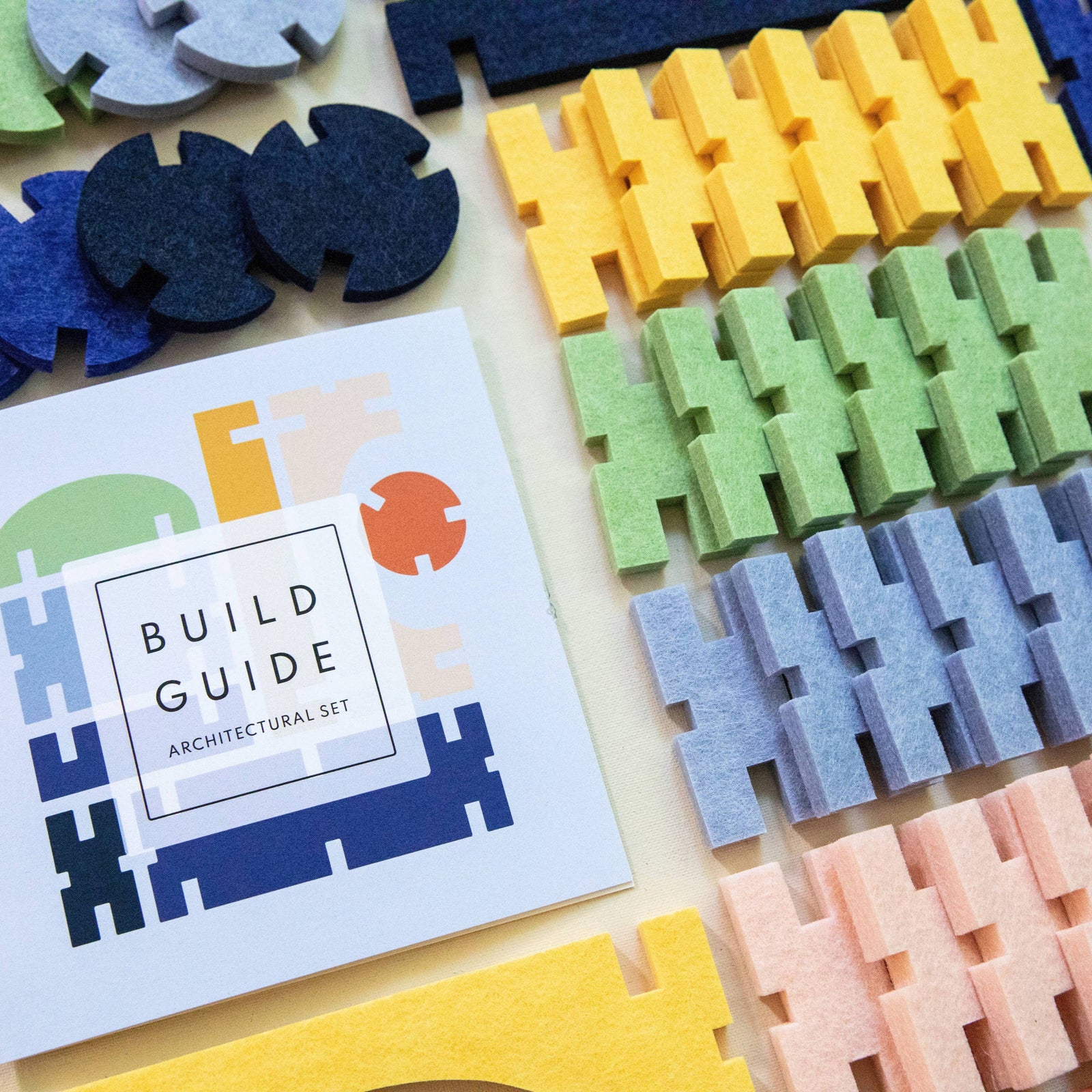 Colorful felt interlocking pieces on a white background with a small book titled 'Build Guide'.