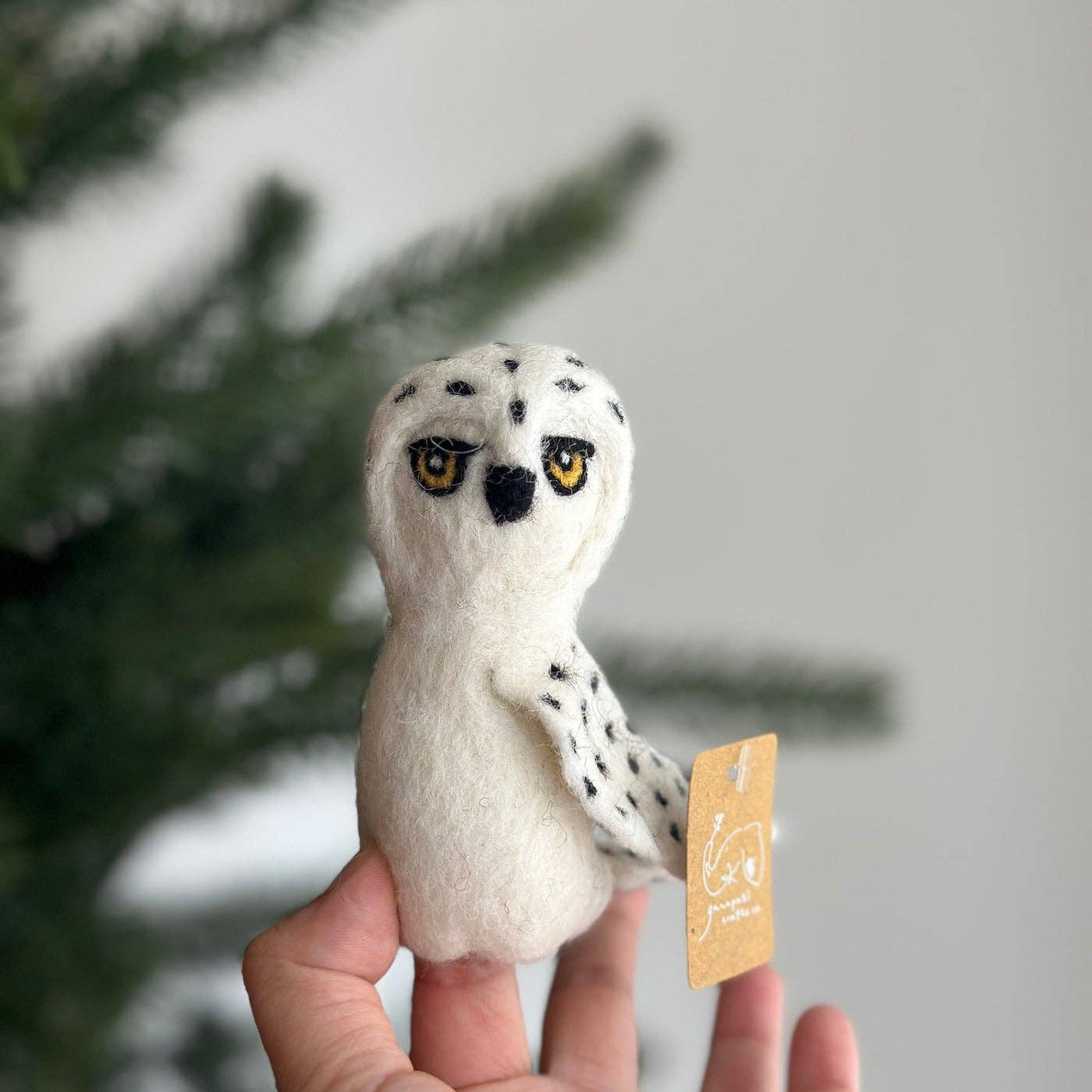 Small white owl plush toy with black spots held in a hand against a blurred green background