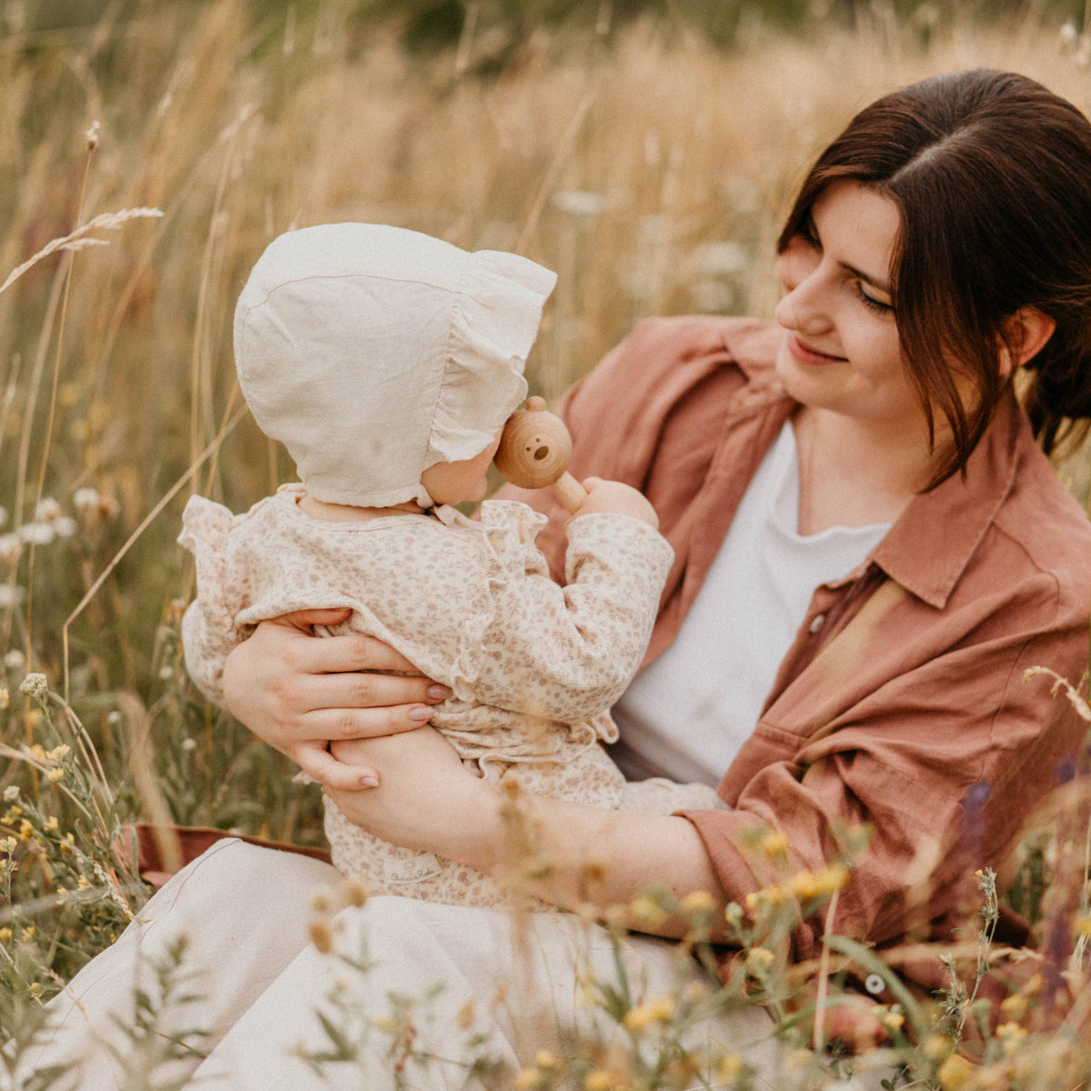 Woman holding a baby in a field of tall grass and wildflowers
