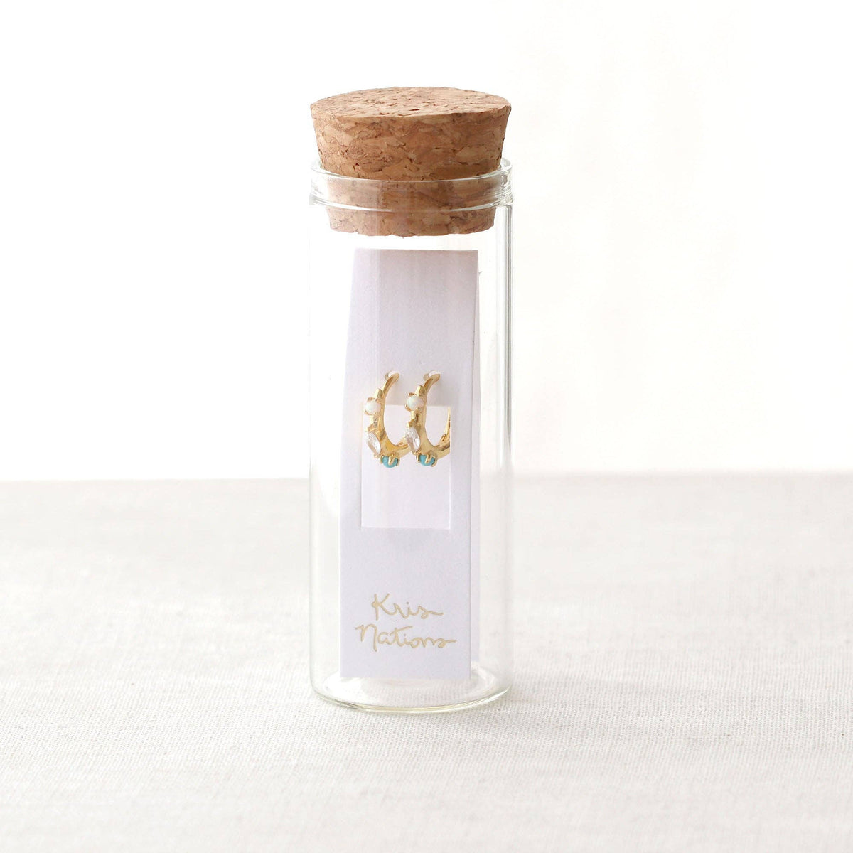 Glass bottle with cork lid containing earrings on a white background