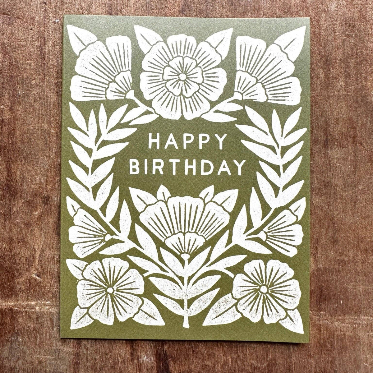 Green birthday card with white floral designs on a wooden surface