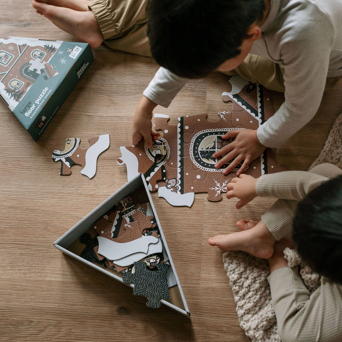 Two children playing with a puzzle on a wooden floor