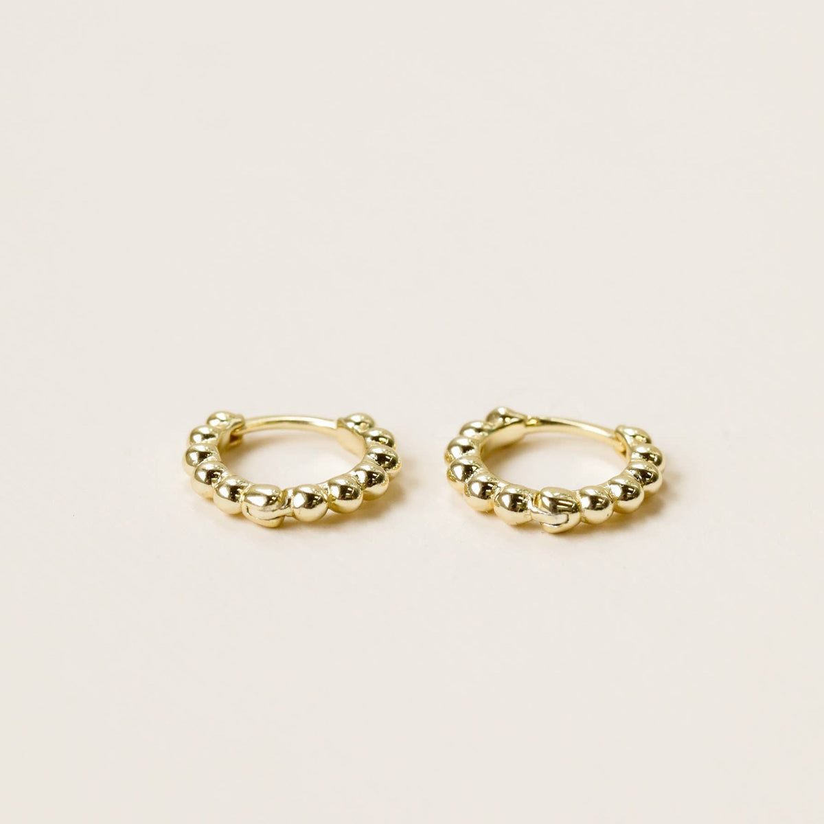 A pair of small gold-colored ball hoop earrings with curved ear wires and snap closures on a plain background.