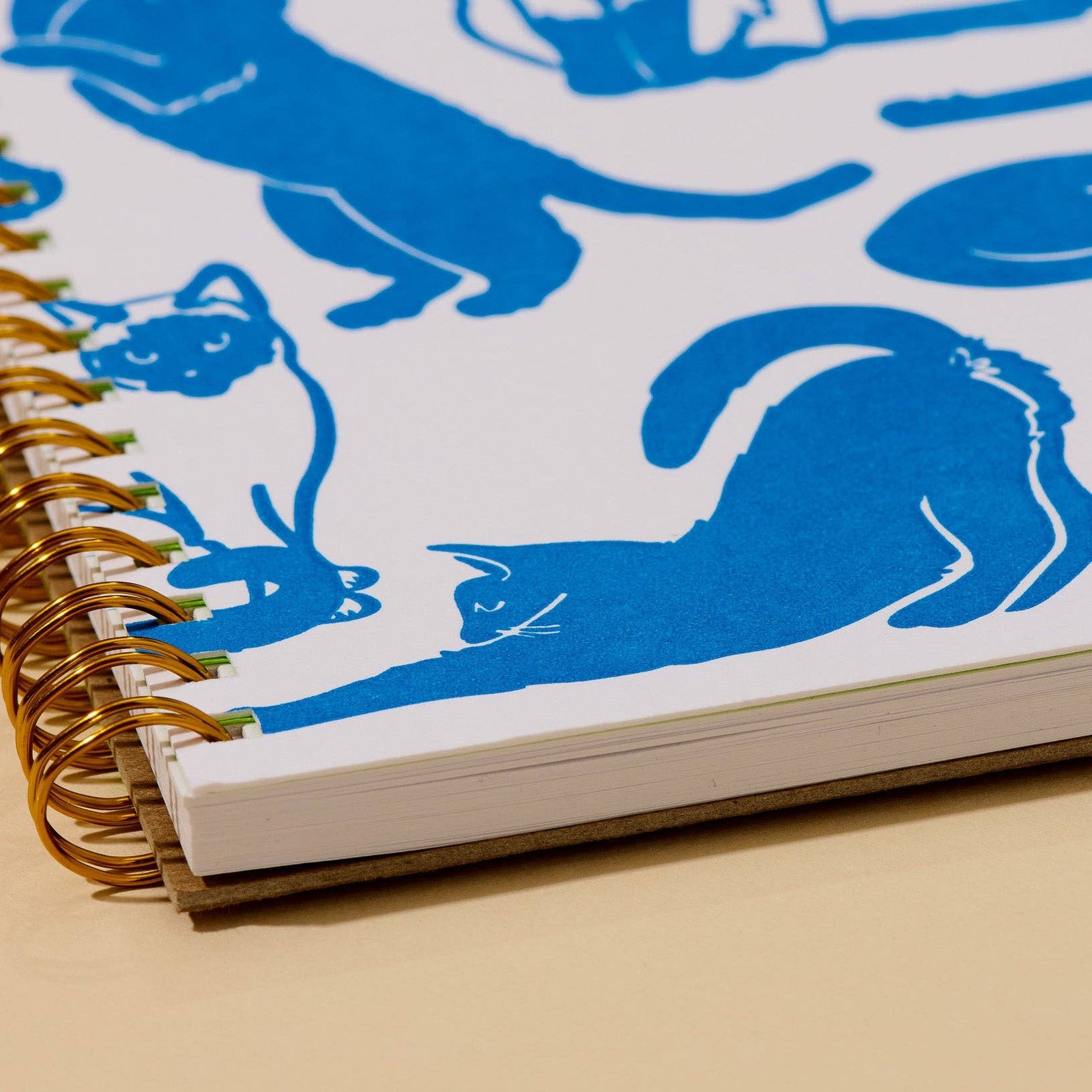 A spiral-bound notebook with a white cover decorated with blue cat illustrations and a bright green front cover that reads 'AND HERE WE ARE! NOTEBOOK'.