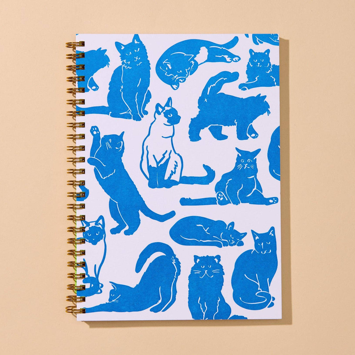 A spiral-bound notebook with a white cover decorated with blue cat silhouettes, photographed on a warm beige background.