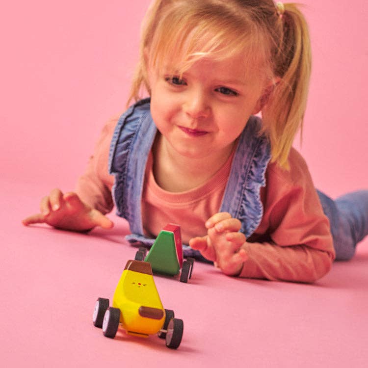 Wooden toy cars shaped like a watermelon, banana, and avocado on a white background