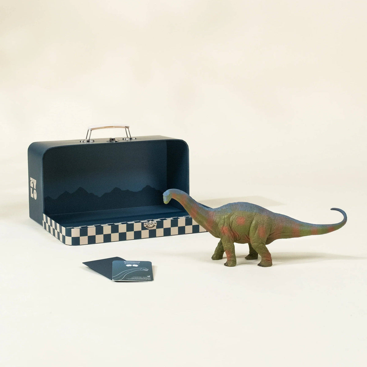 Toy dinosaur next to an open suitcase with a checkered interior on a beige background