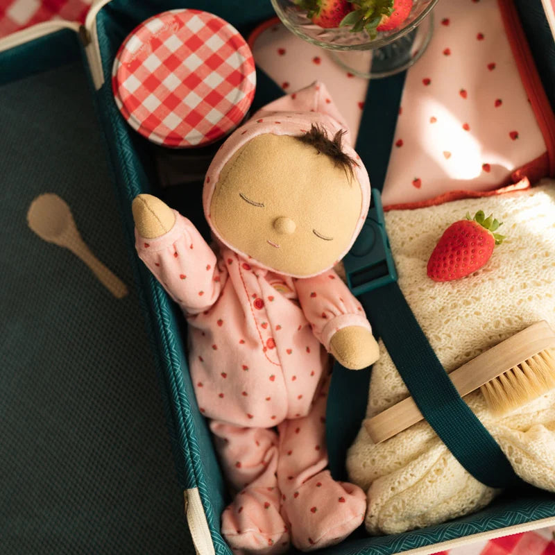Stuffed toy in a green box with a wooden spoon, sponge, and strawberry on a checkered tablecloth.