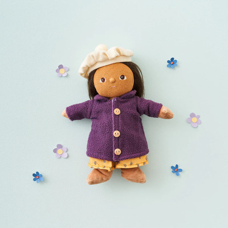 Toy doll wearing a purple coat and white hat , yellow dress on a light blue background with decorative flowers.