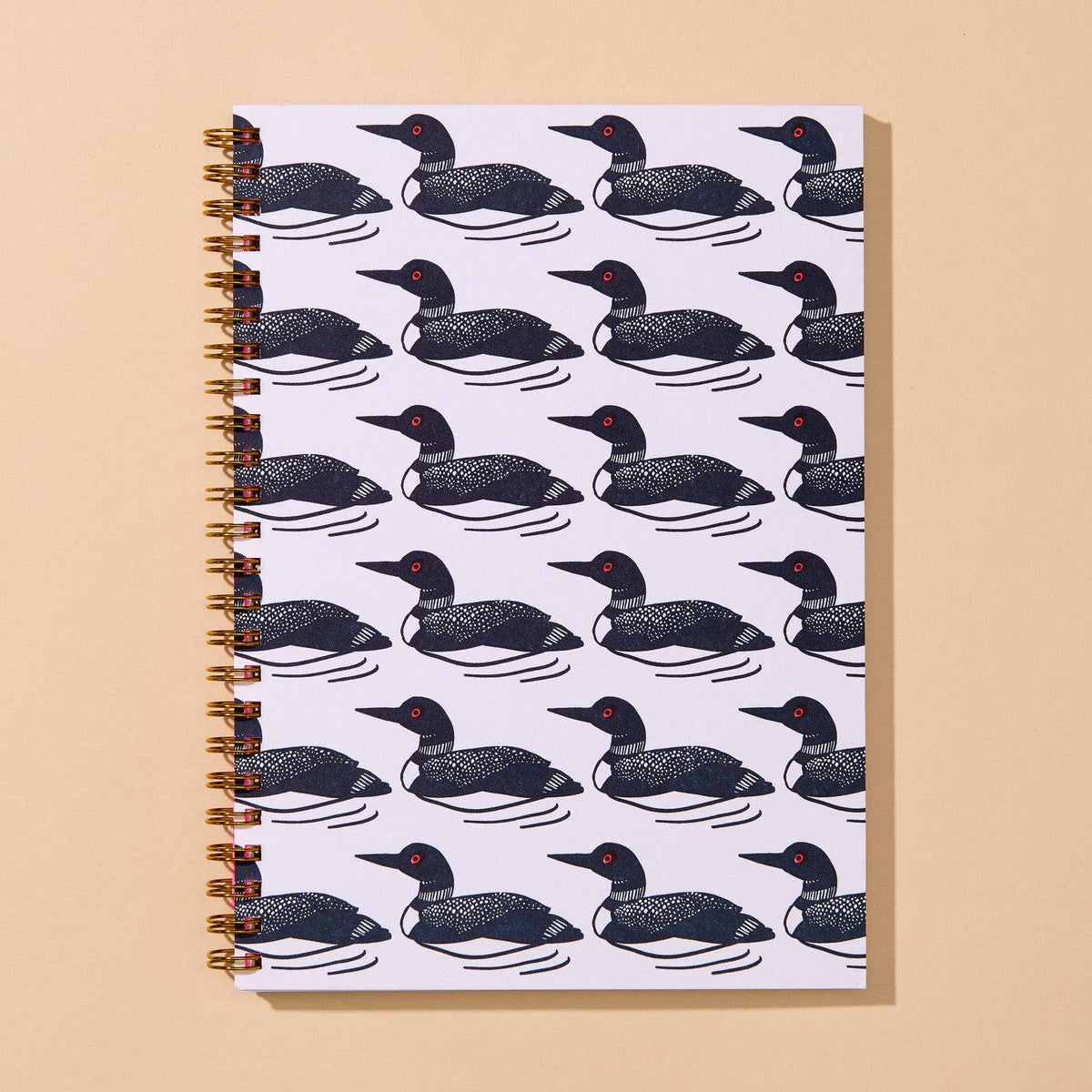 A spiral-bound notebook with a repeating pattern of black and white loons on a white cover, set against a solid beige background.
