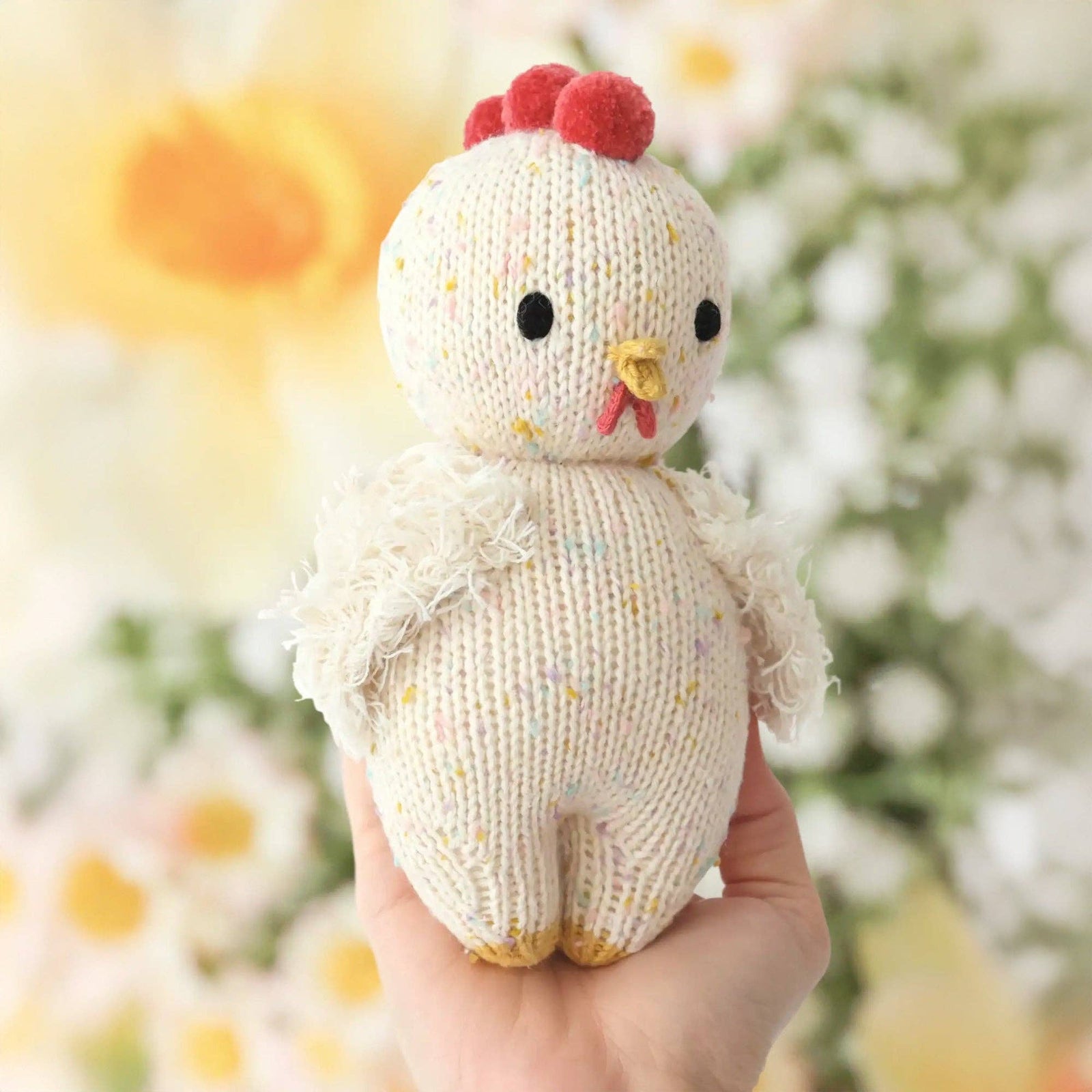 Knitted chicken toy held in a hand with a blurred floral background
