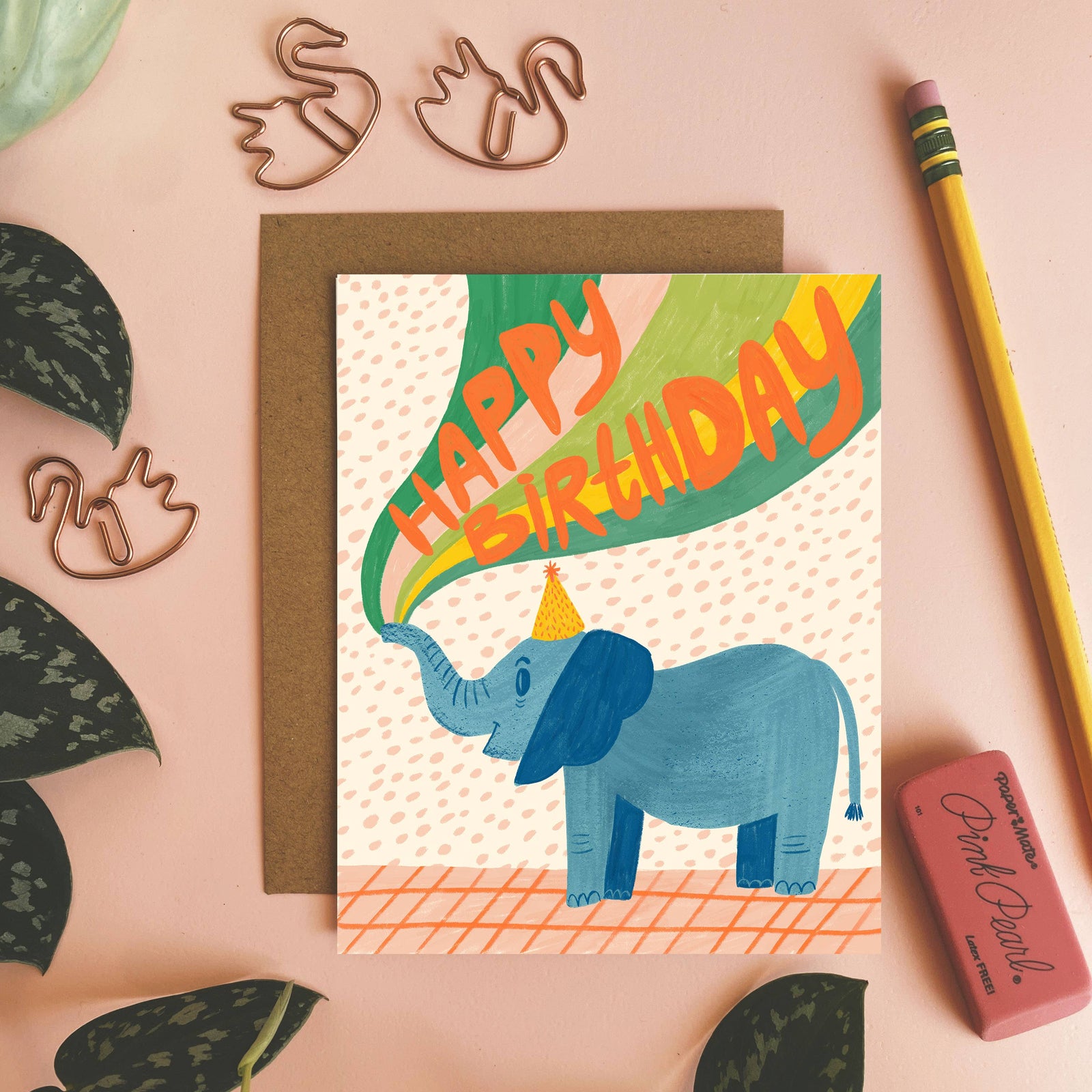 Birthday card with an elephant illustration on a pink surface with decorative elements.