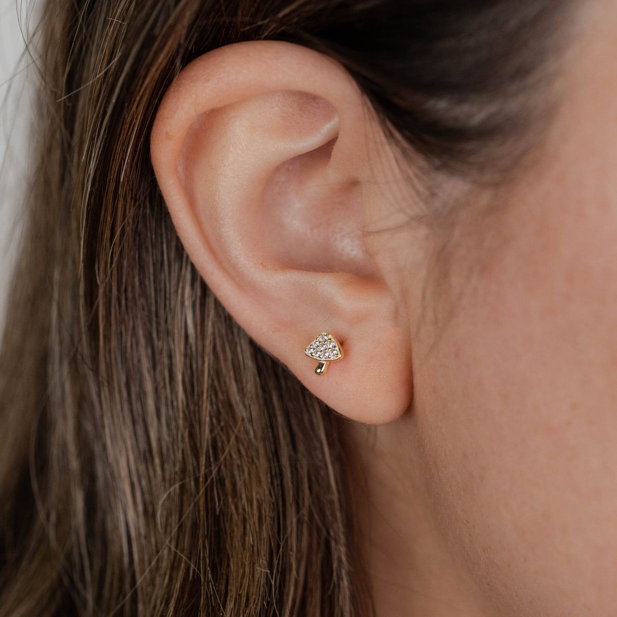 Close-up of an ear wearing a mushroom stud earring with hair partially covering the frame.