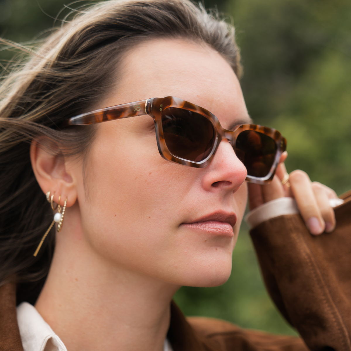 Woman wearing tortoiseshell sunglasses with a blurred green background