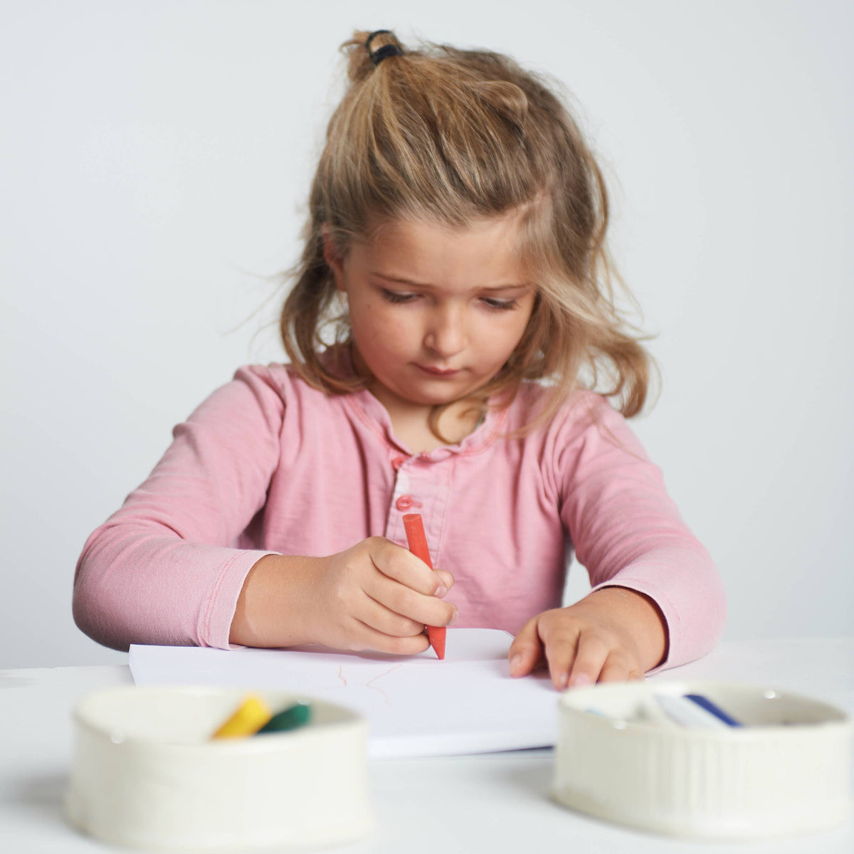 Young girl in a pink shirt writing on paper with a red marker.