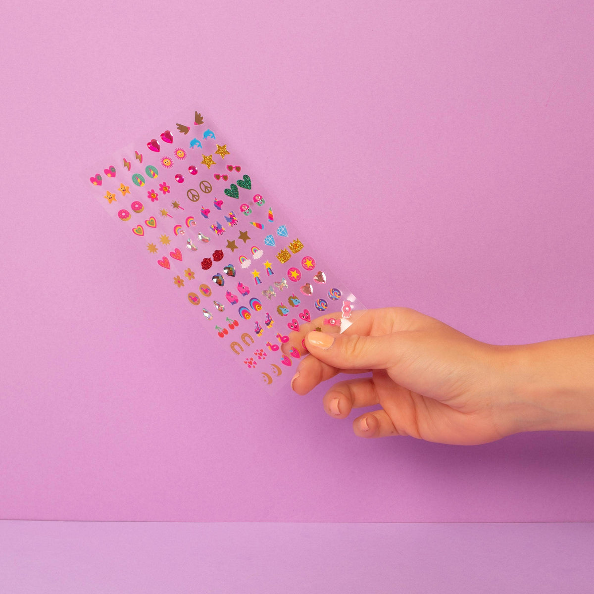 Hand holding a colorful heart-shaped confetti against a pink background