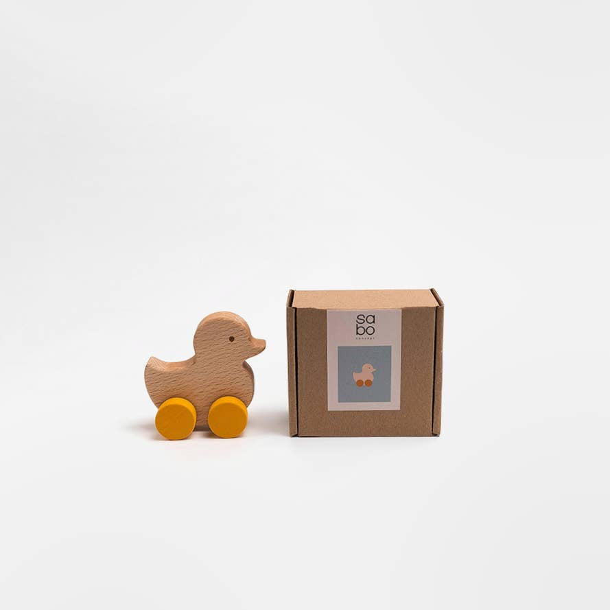 Wooden duck toy with wheels next to its packaging on a white background