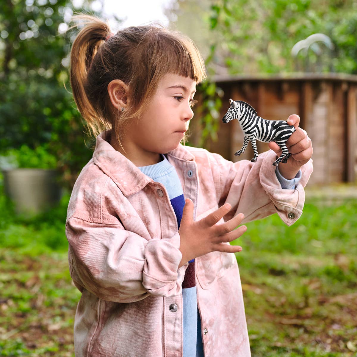 Child holding a toy zebra outdoors with greenery in the background