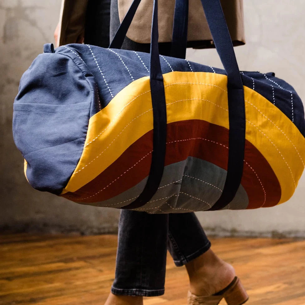 woman carrying large duffle bag with yellowed and grey strips