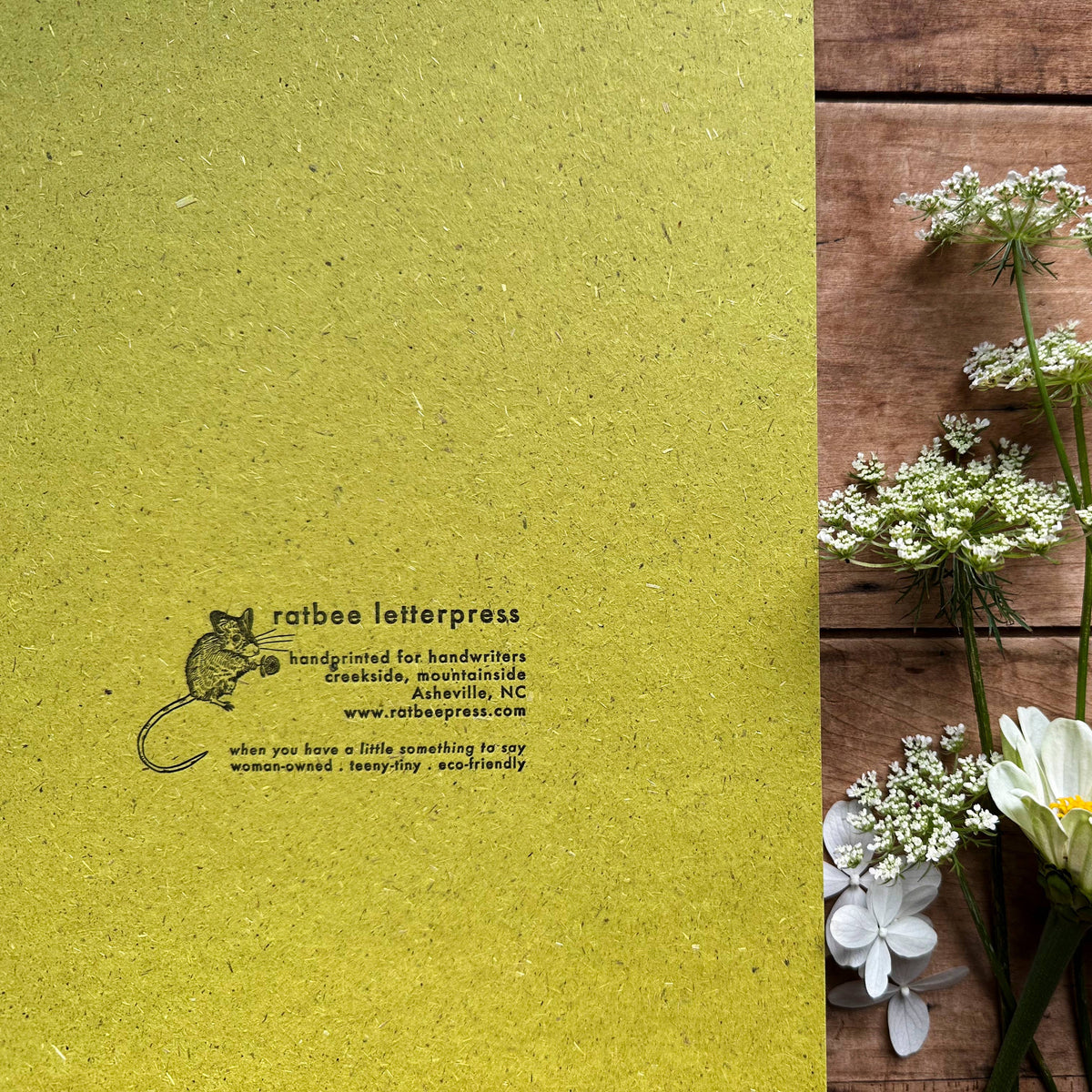 Flowers and scissors on a wooden surface with a green letterpress label.