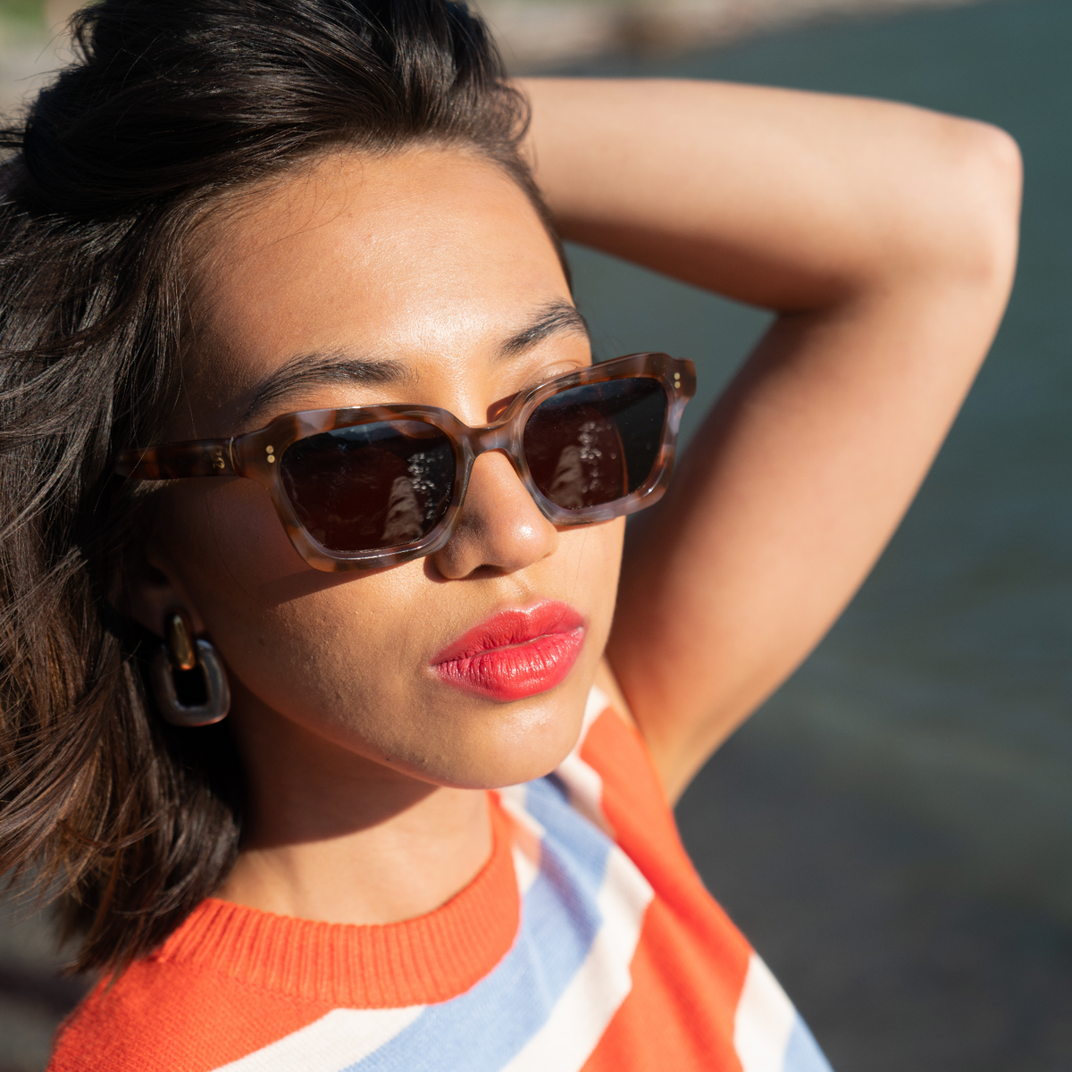 Woman wearing sunglasses and a striped sweater by a body of water
