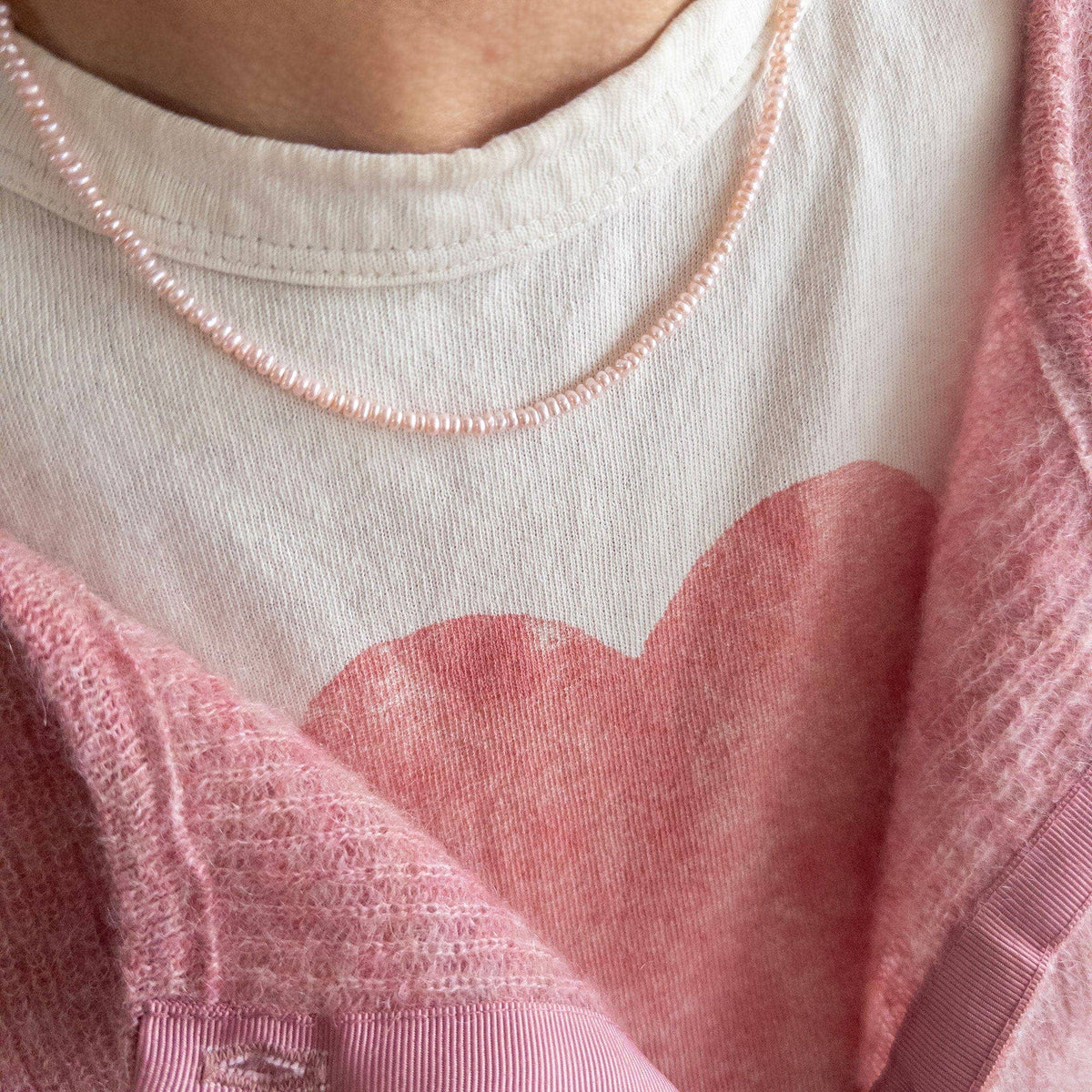 Close-up of a person wearing a pink cardigan over a white shirt with a pink pearl necklace