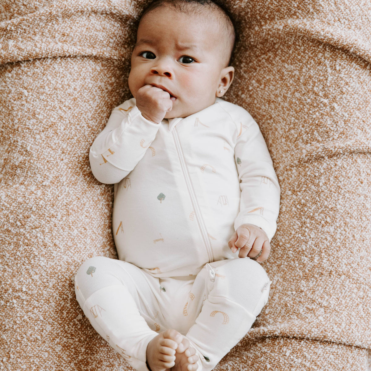 Baby in a white onesie lying on a textured brown blanket